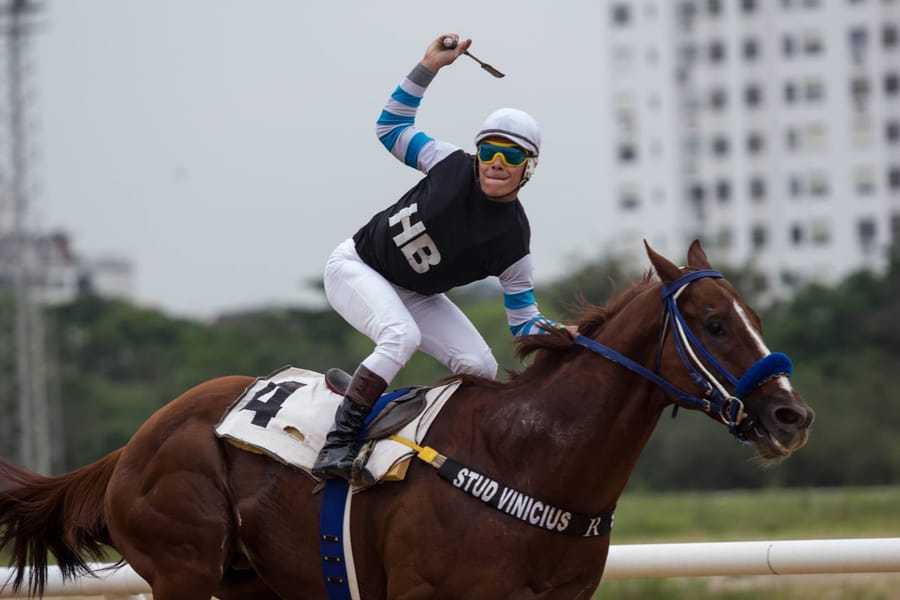 Jóquei de blusa preta com mangas listradas comemora a vitória sobre o cavalo número 4 na reta do Cristal